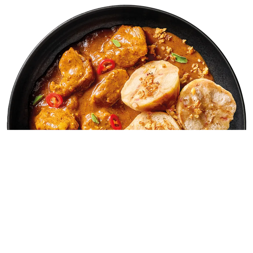 Guláš s kousky masa v omáčce, podávaný s knedlíky a plátky červené papriky.