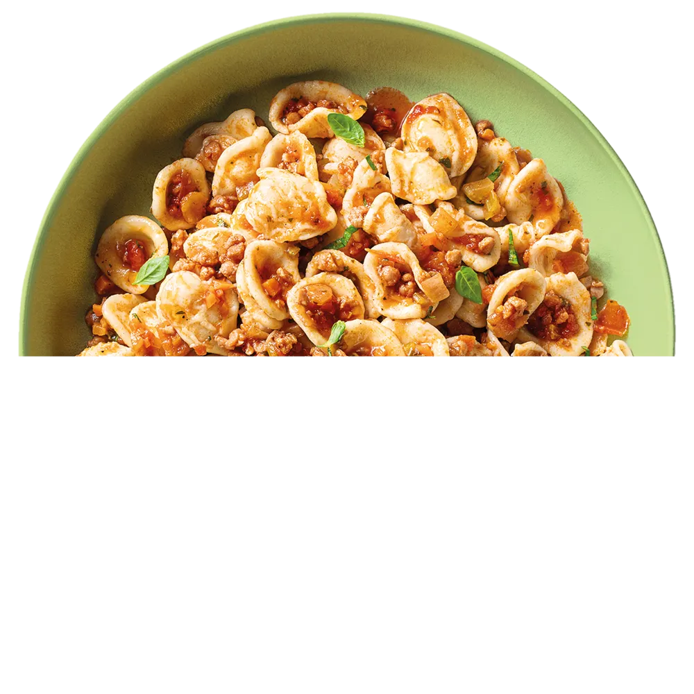 Talíř zelených těstovin orecchiette s boloňskou omáčkou a několika lístky bazalky.