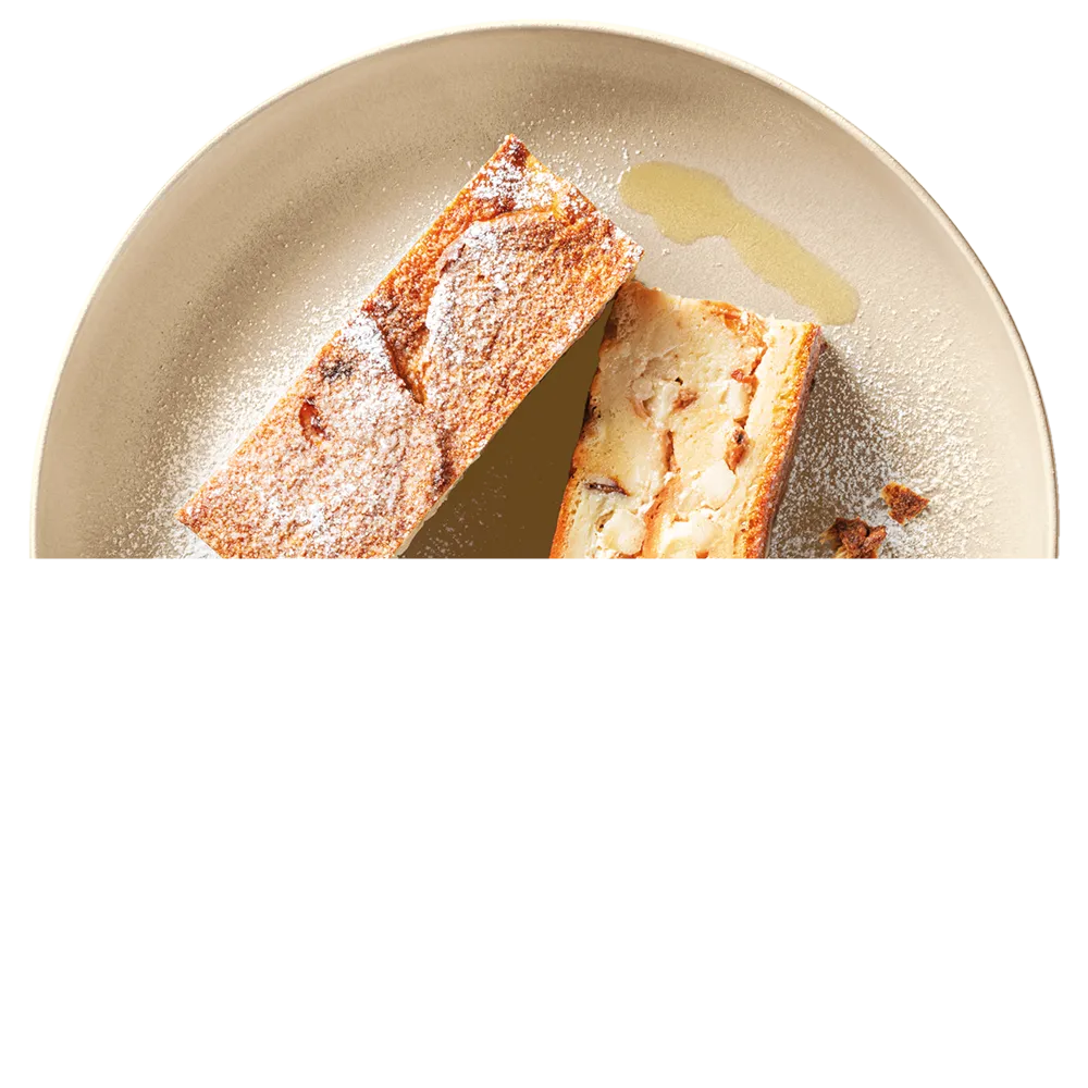 Dva kousky pečeného dezertu posypané moučkovým cukrem na talíři s trochou sirupu.