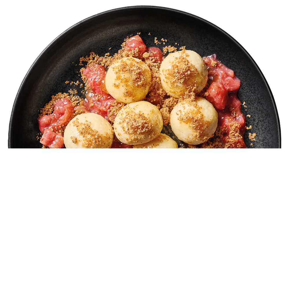 Černý talíř s pěti tvarohovými noky posypanými drobenkou a podávanými s červenou ovocnou omáčkou.