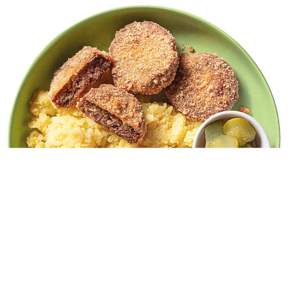 Smažené karbanátky s bramborovou kaší a nakládanými okurkami na zeleném talíři.