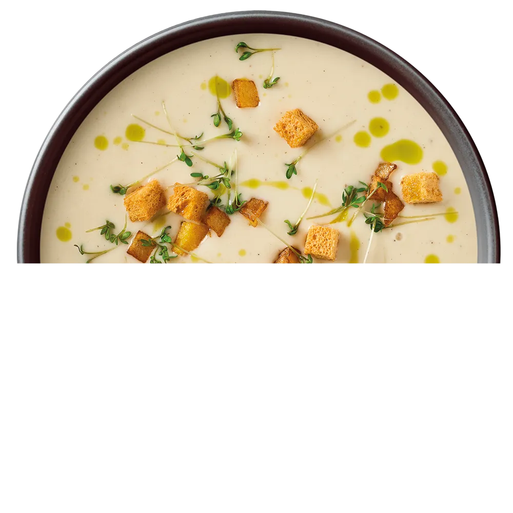 Miska krémové polévky ozdobená krutony, zelenými bylinkami a kapkami olivového oleje.