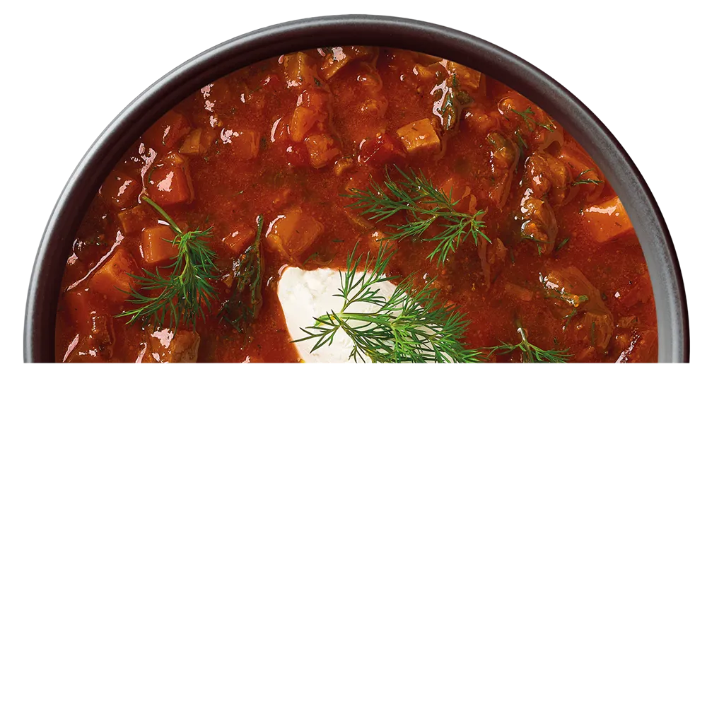 Červená polévka s kousky zeleniny, smetanou a bylinkami v misce.