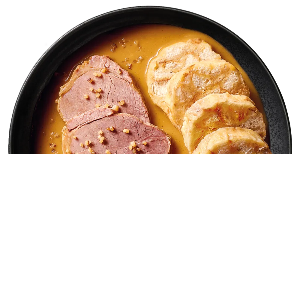 Černý talíř s plátky hovězí svíčkové v hnědé omáčce a krájenými houskovými knedlíky.