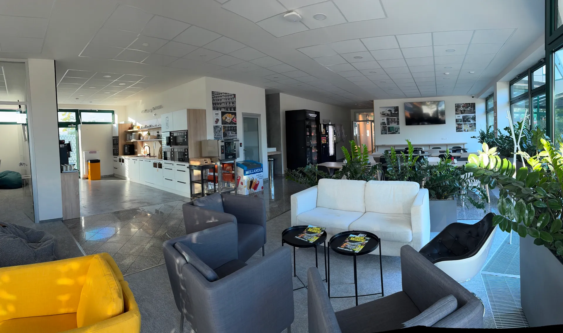 Moderní kancelářská kuchyňka a odpočinková zóna s pohodlnými křesly, pohovkou a velkými okny s výhledem ven.