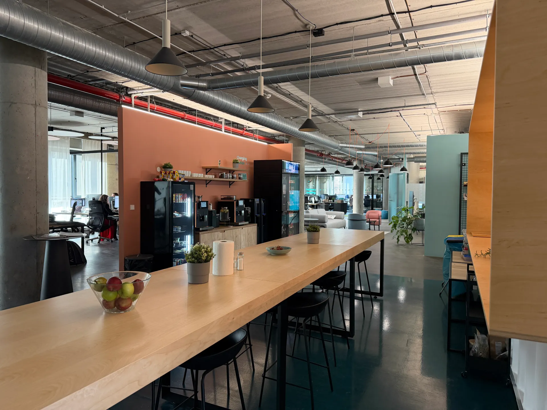 Černý automat na čerstvé jídlo s prosklenými dvířky zobrazujícími balené pokrmy v kancelářském prostoru vedle coffee baru.