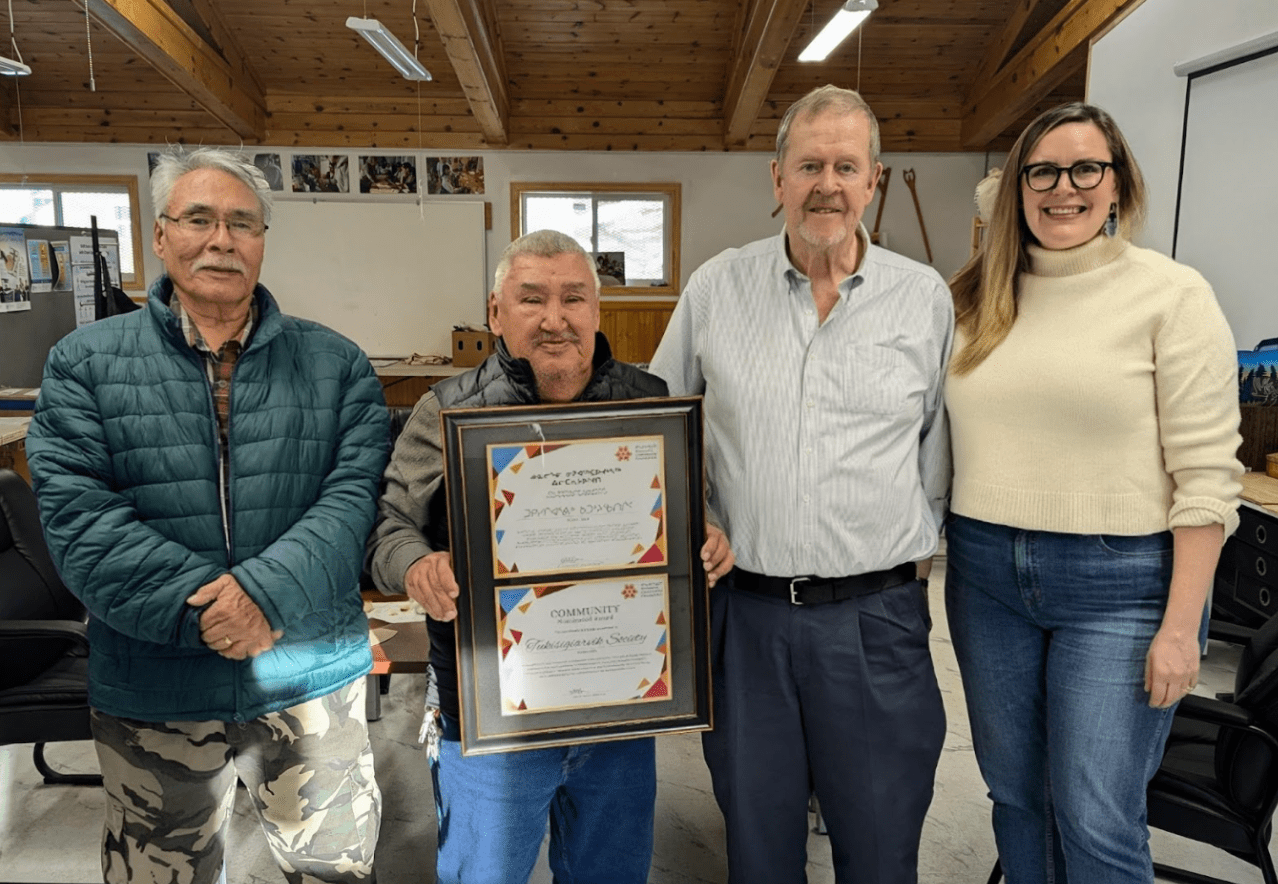 Four people in a row, with a man holding up a certificate in the middle.