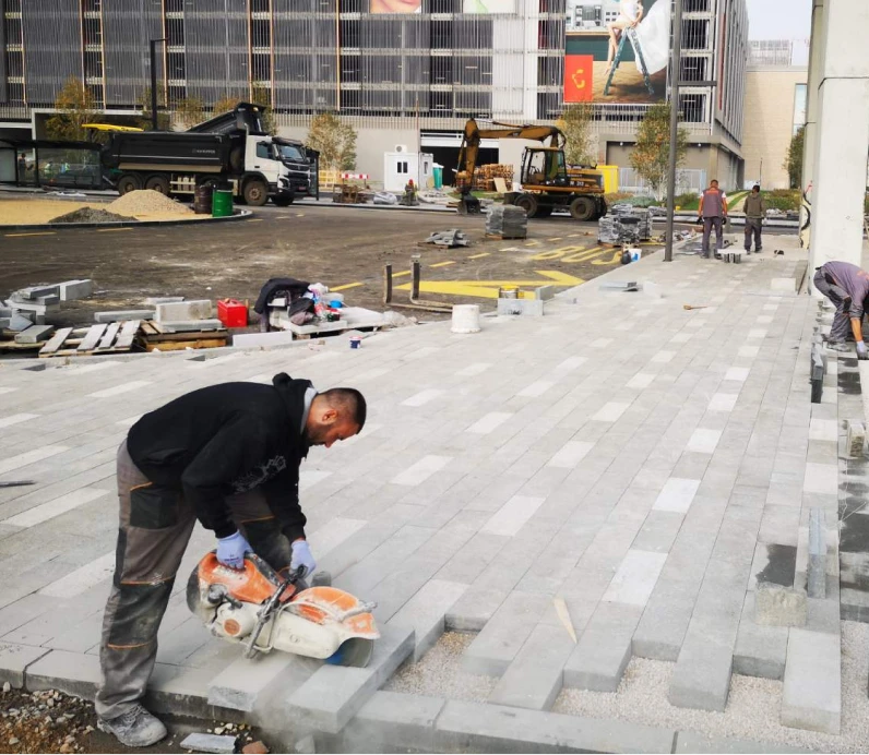 Construction worker cutting paving stones with a power saw on an outdoor sidewalk.