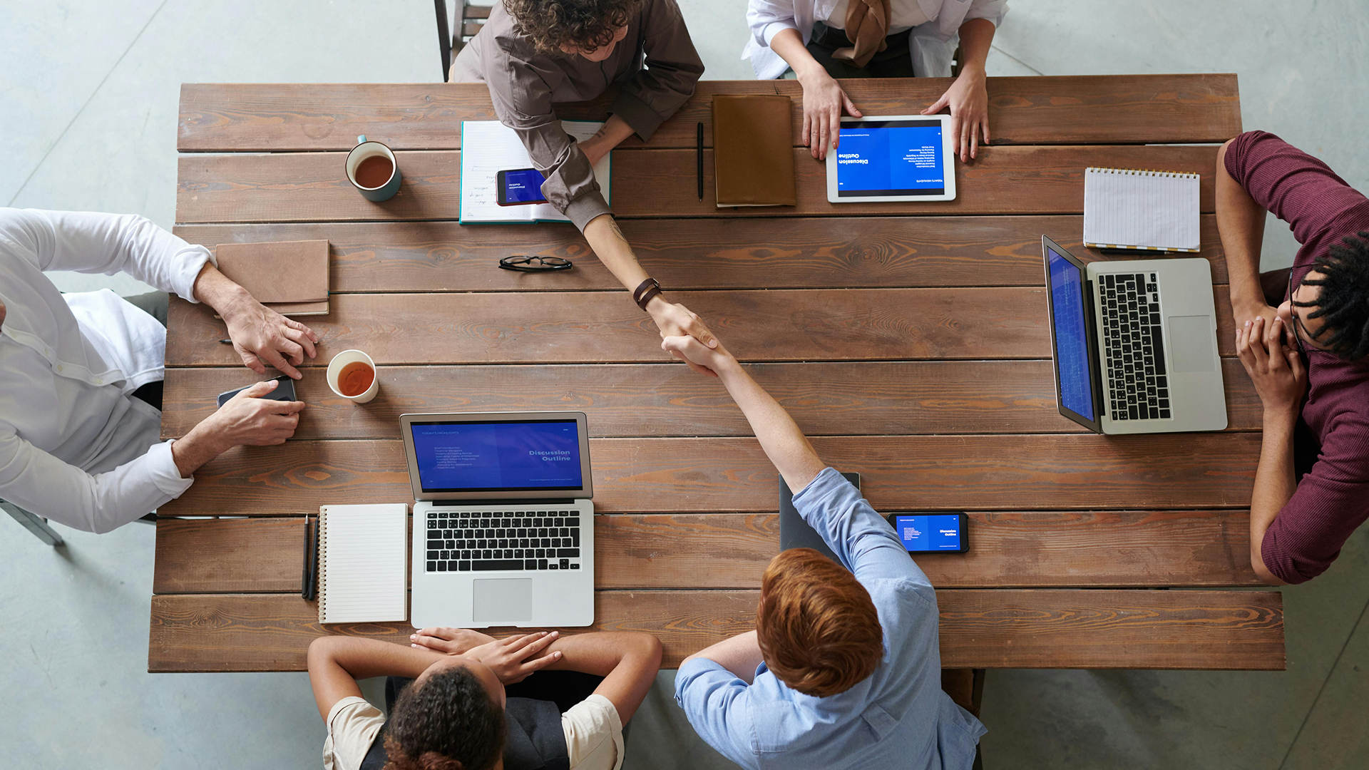 Team working together over a desk, computers open and hands shaking.