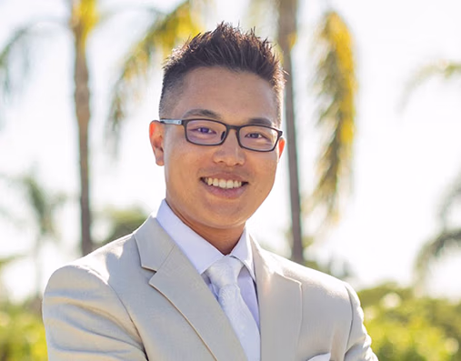 Headshot of Dr. Trace Huang smiling outdoors in a light beige suit.
