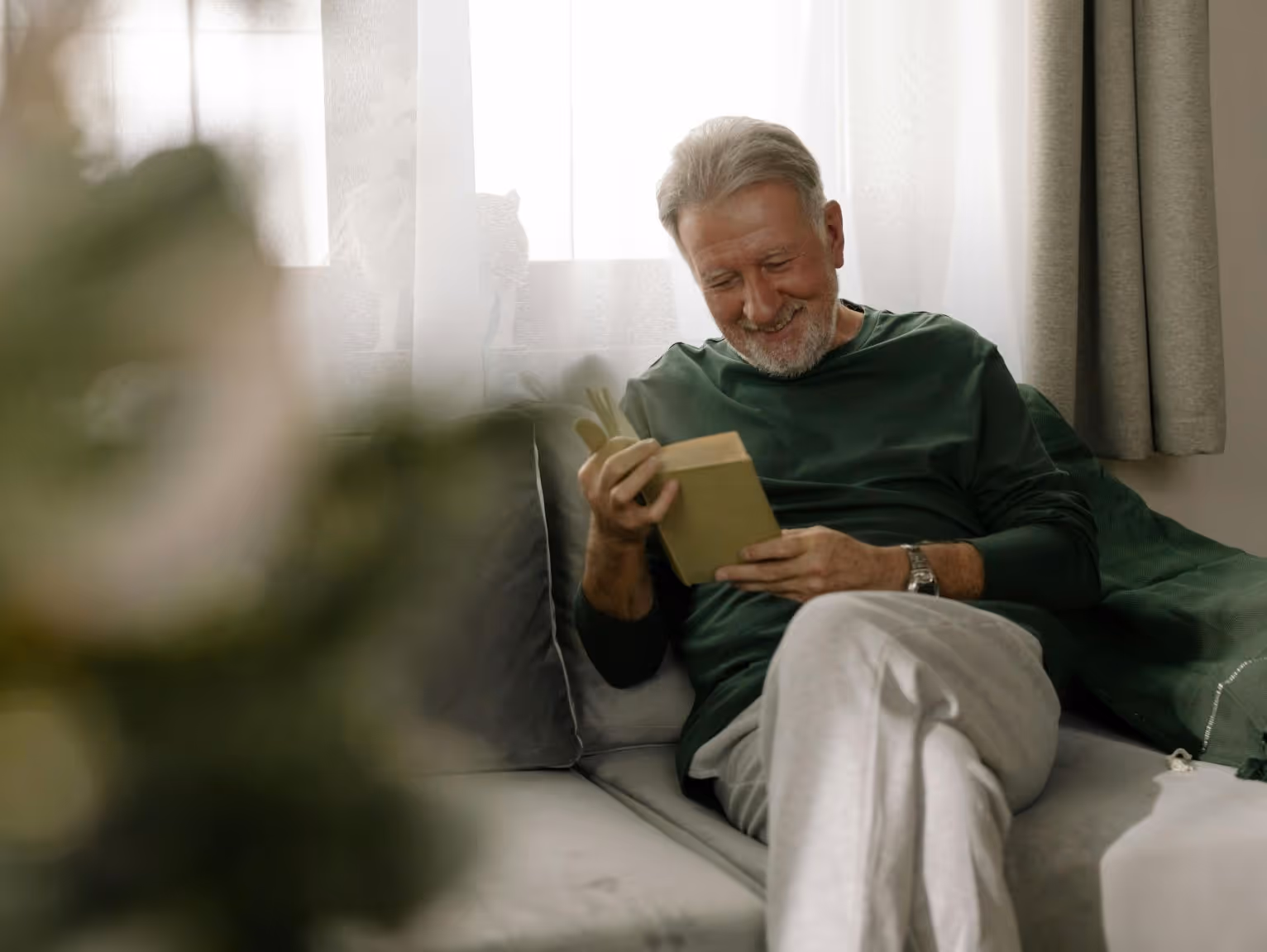 Elderly man sitting on a couch reading a book, receiving ongoing care for schizophrenia.