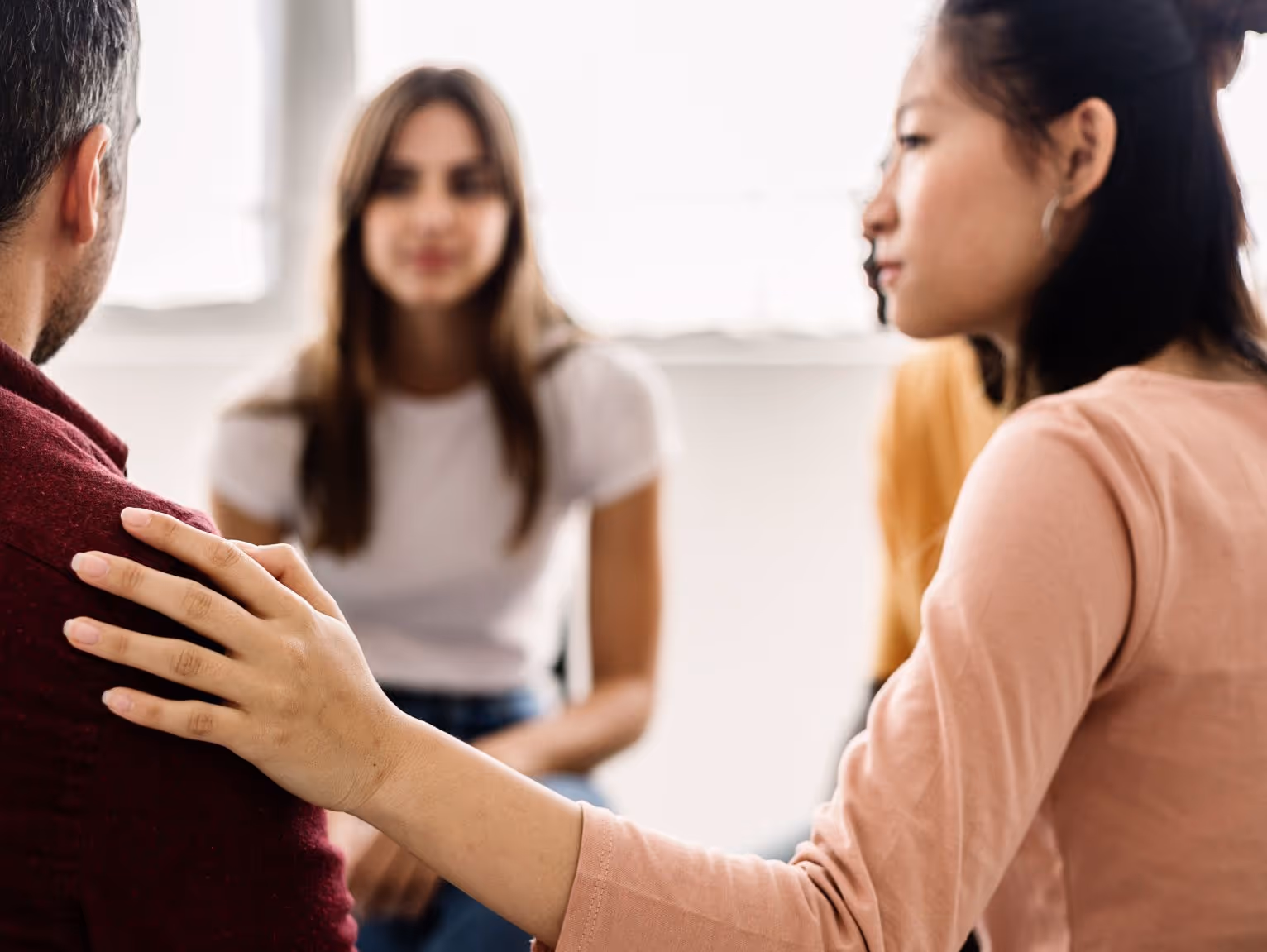 Woman gently placing hand on a man's shoulder in a trauma support group therapy session.
