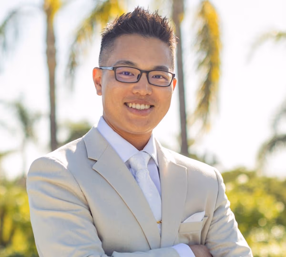 Headshot of Dr. Trace Huang smiling outdoors in a light beige suit.