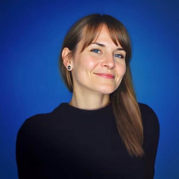 Woman with straight brown hair and blue eyes wearing a black top against a blue background.