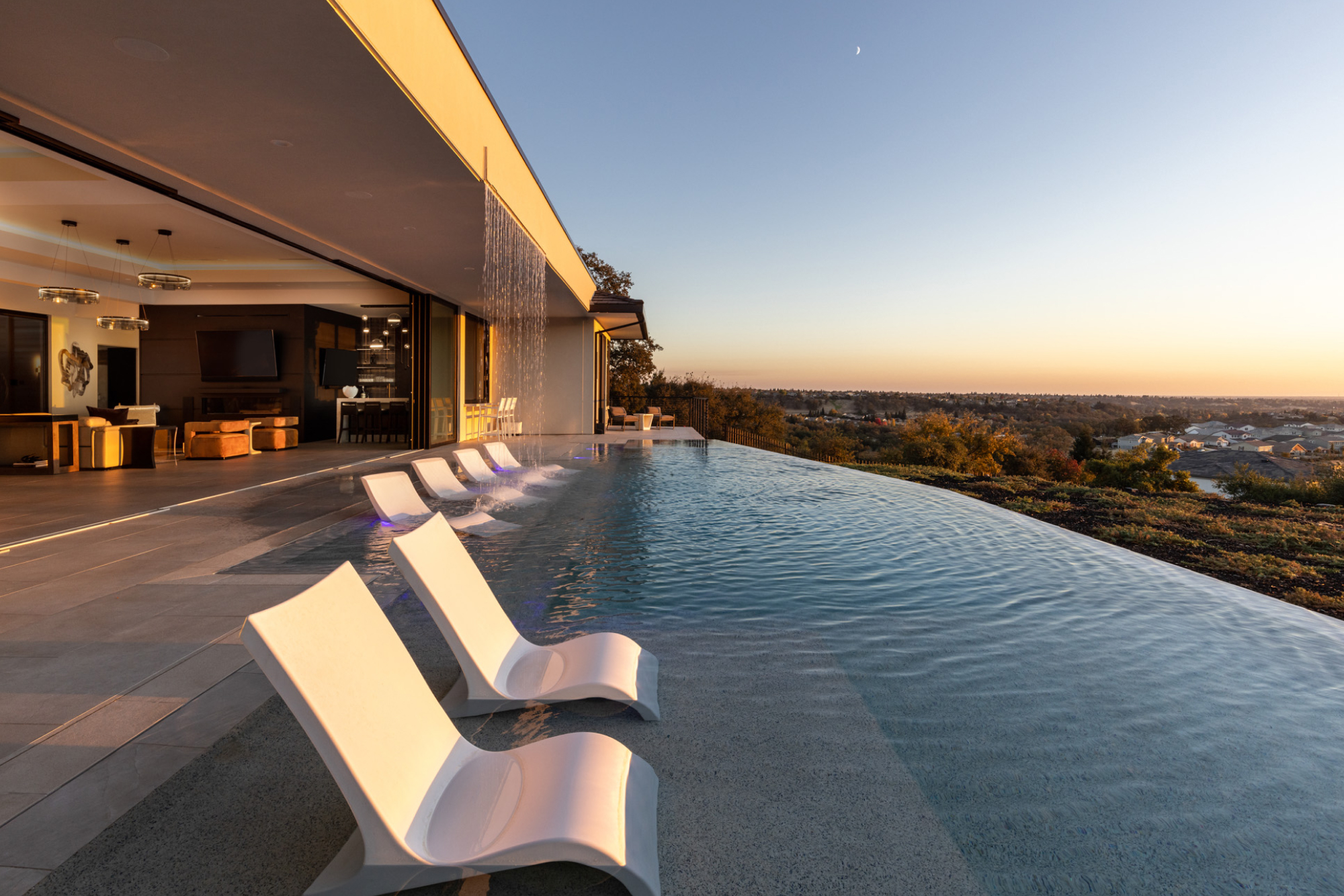 Modern outdoor space with infinity pool and lounge chairs, overlooking Lincoln, CA at sunset.