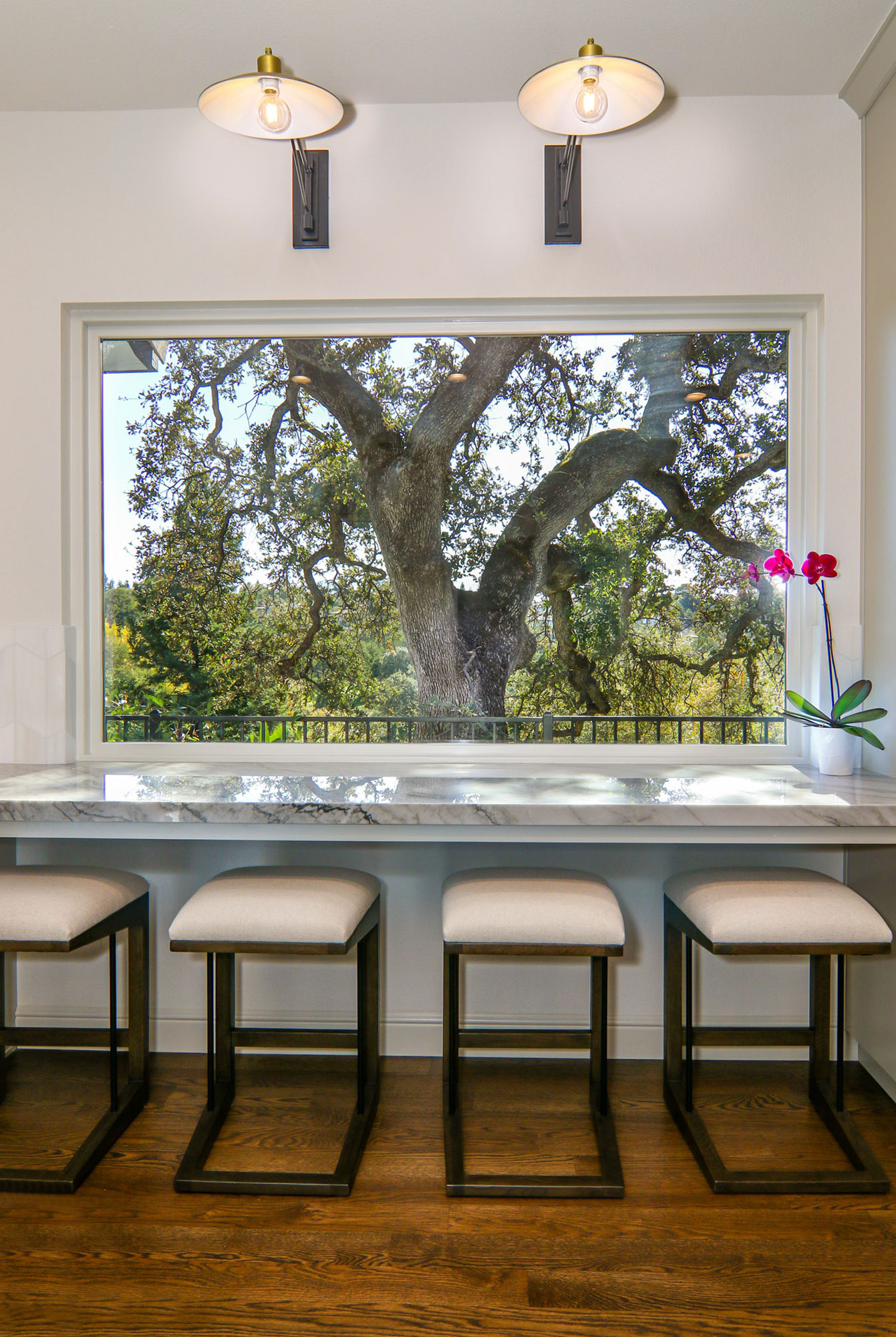 Modern kitchen remodel in Roseville, CA with marble countertop, cushioned stools, and natural light from a large window.