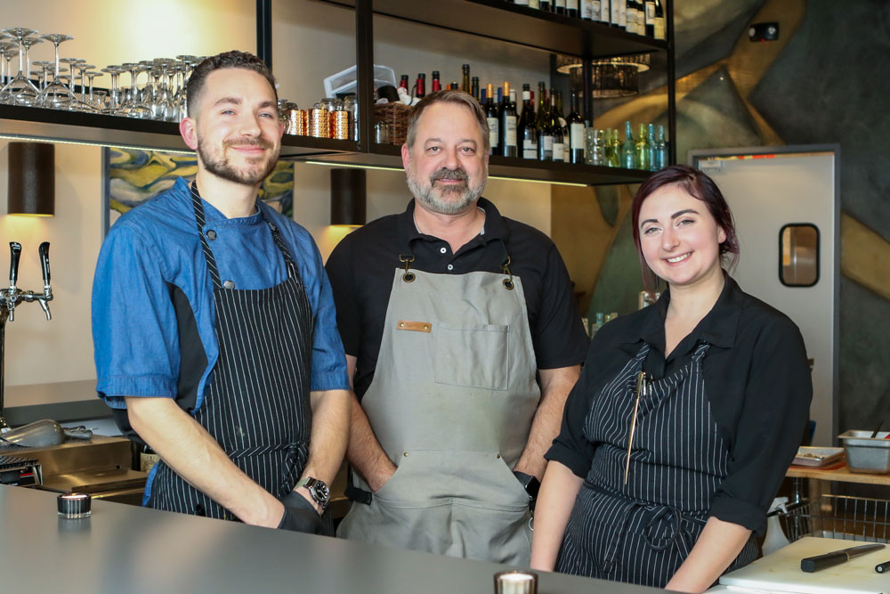 Three chefs posing in a modern restaurant kitchen in Lincoln, CA, showcasing contemporary design elements and a vibrant atmosphere.