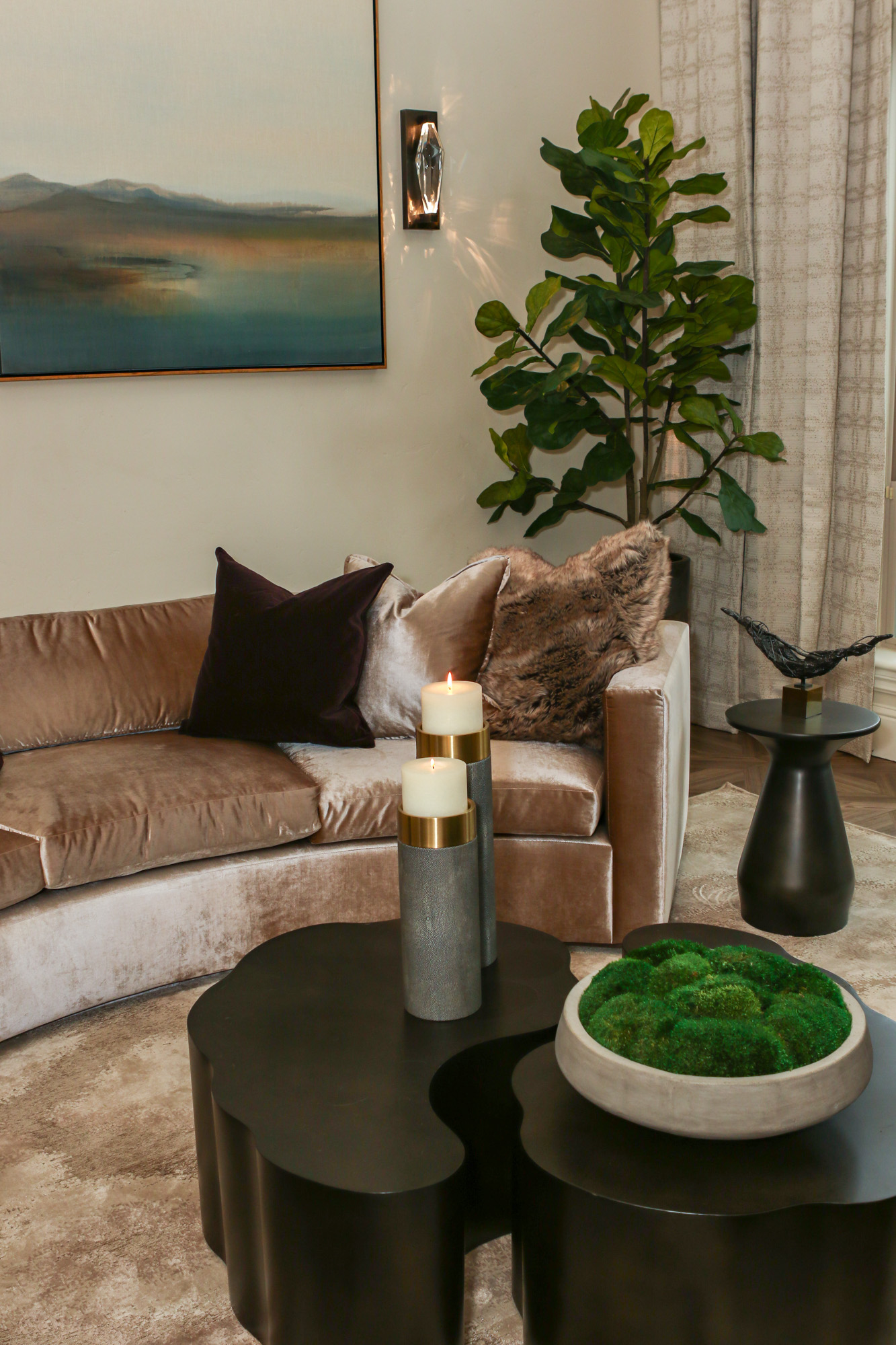 Modern living room in Lincoln, CA featuring a curved velvet sofa, unique coffee tables, candles, and decorative plants.