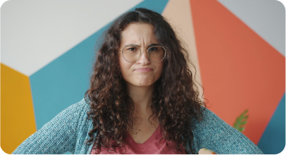 Young woman with curly hair and glasses looking confused with a colorful geometric background.