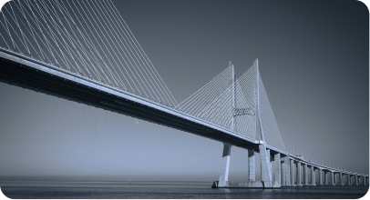 Long cable-stayed bridge extending over calm water under a clear sky.