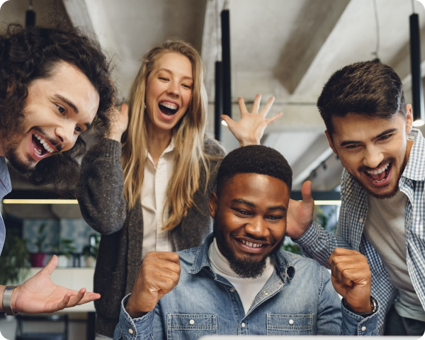 Four diverse coworkers celebrating with smiles and raised fists in a modern office.