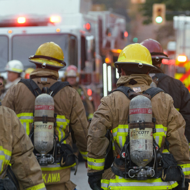 Firefighters in full gear walking towards emergency vehicles with lights flashing.