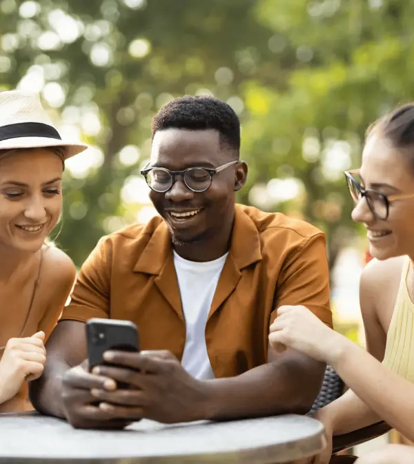 A group of people sitting around a table looking at a cell phone.