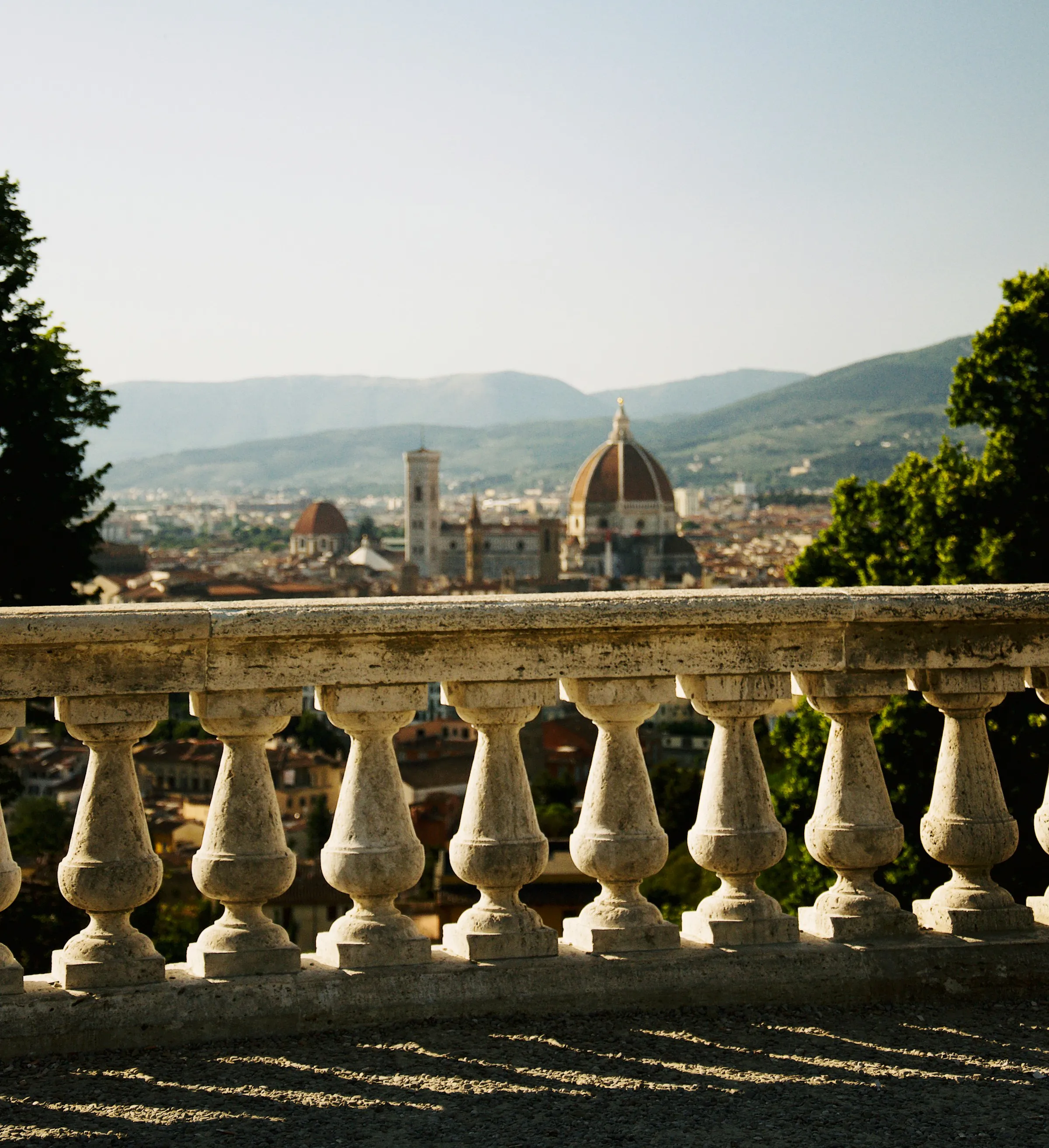 Stone balustrade in foreground overlooking Florence cityscape with the Cathedral of Santa Maria del Fiore and surrounding hills in the background.