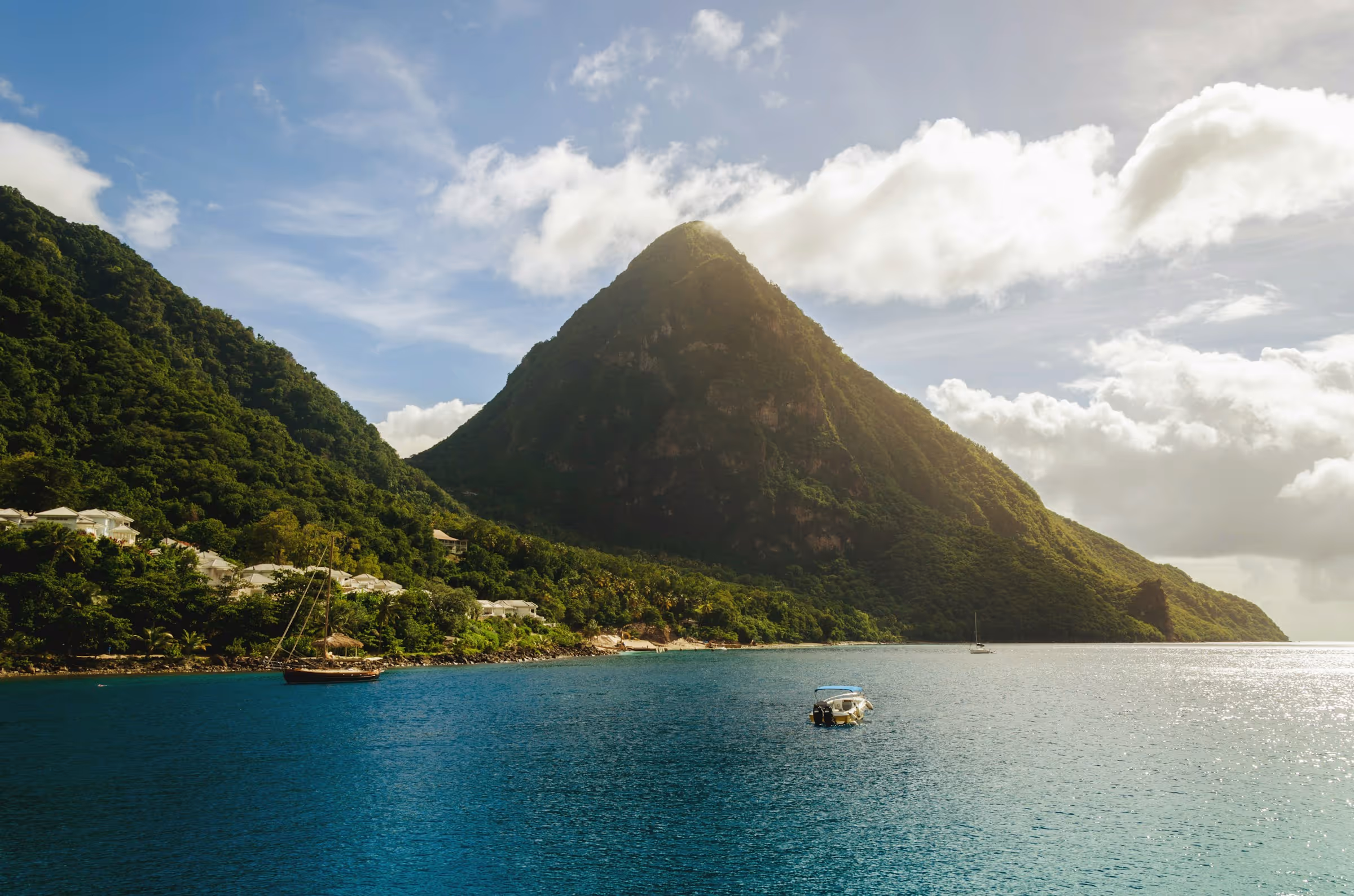 Two lush green mountains with a small boat floating on calm blue water under a partly cloudy sky.