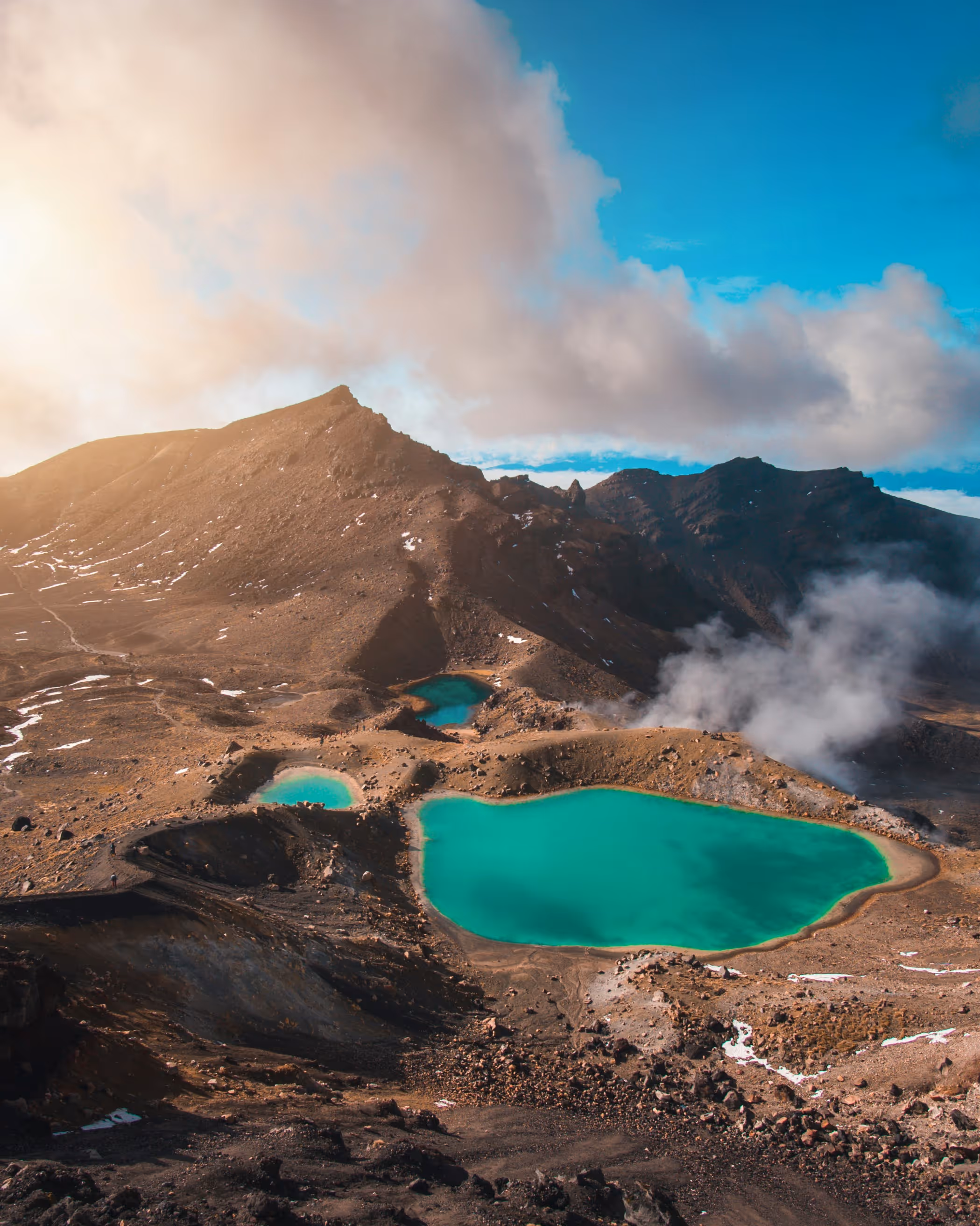 Bright turquoise volcanic crater lakes surrounded by rocky mountain terrain under a partly cloudy sky.