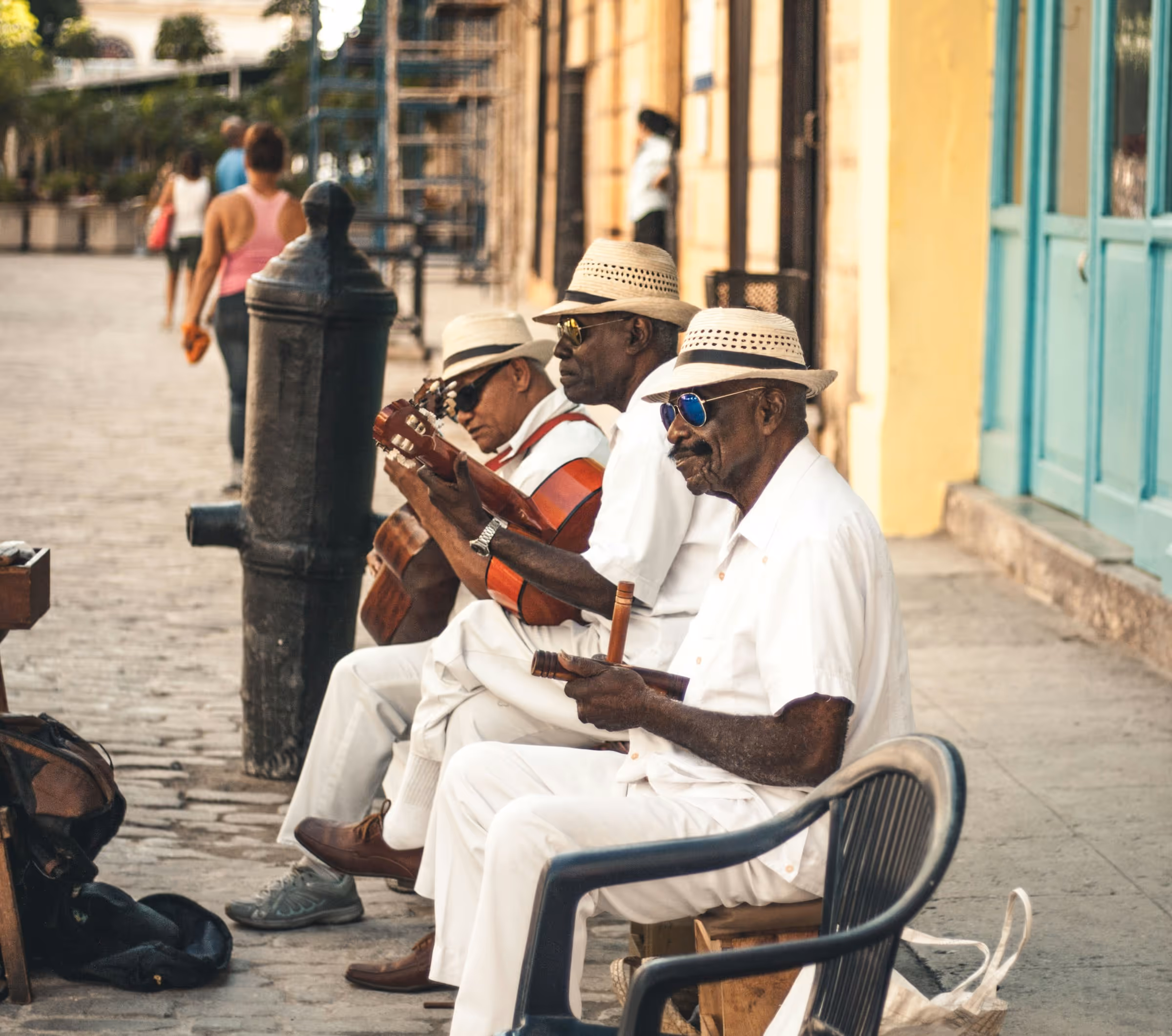 Three elderly men wearing white outfits and hats playing string instruments on a cobblestone street.