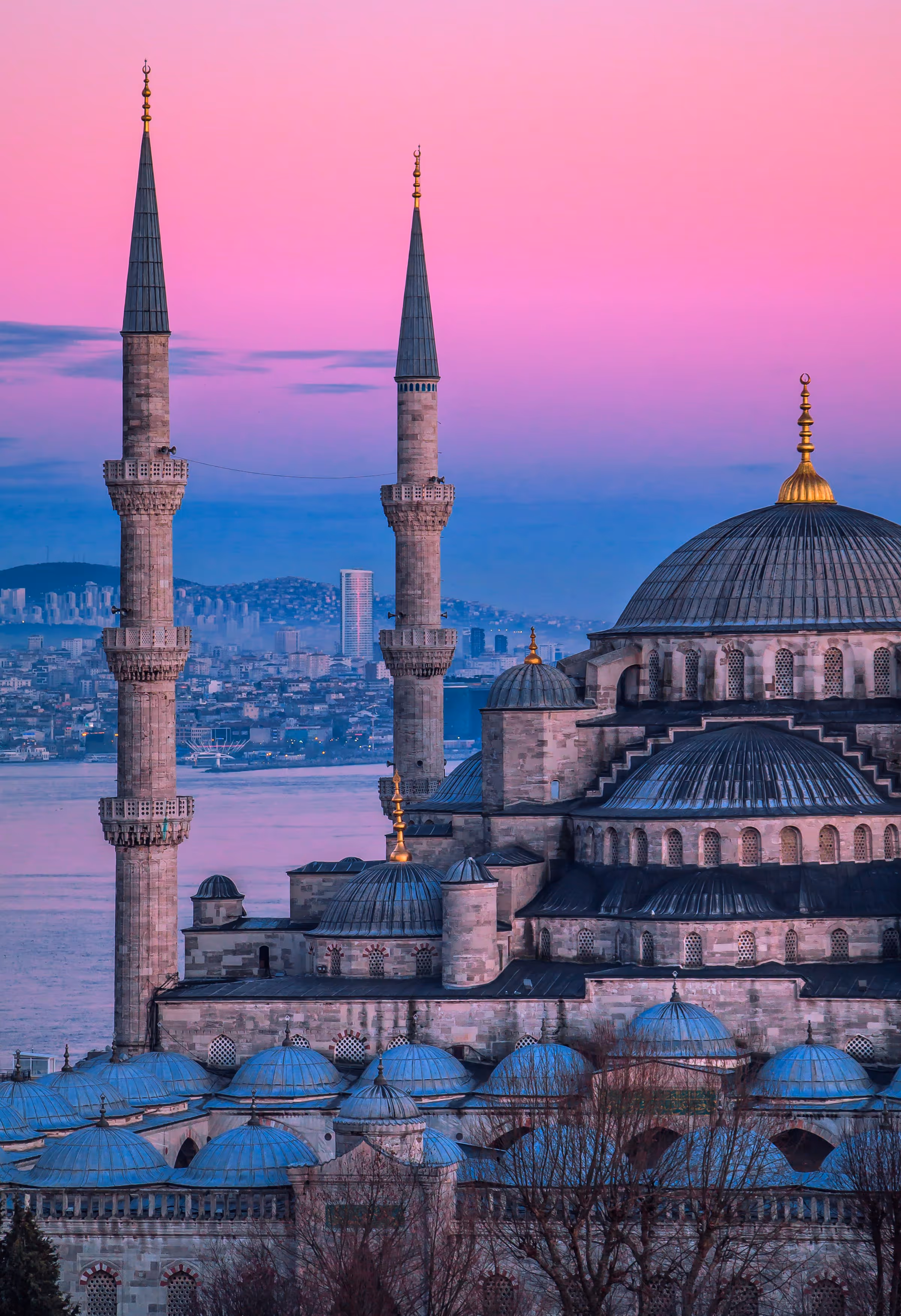 The Blue Mosque in Istanbul at sunset with a pink and purple sky and the cityscape in the background.