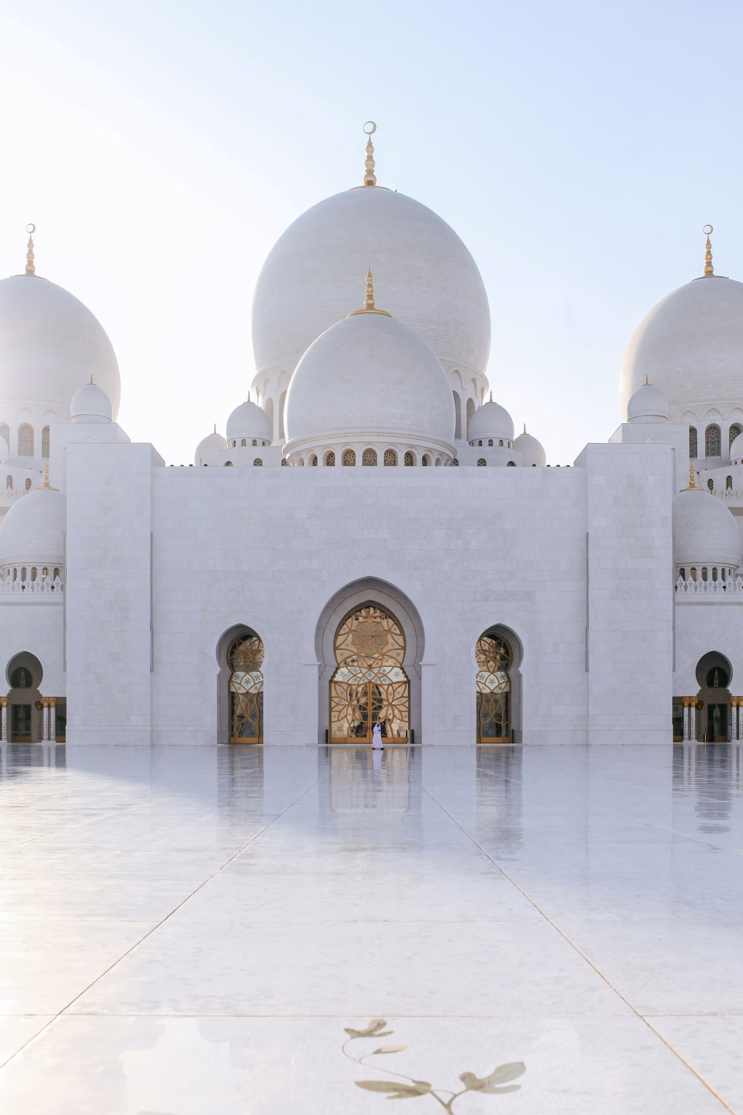 Front view of Sheikh Zayed Grand Mosque with its large white domes and reflective marble courtyard.