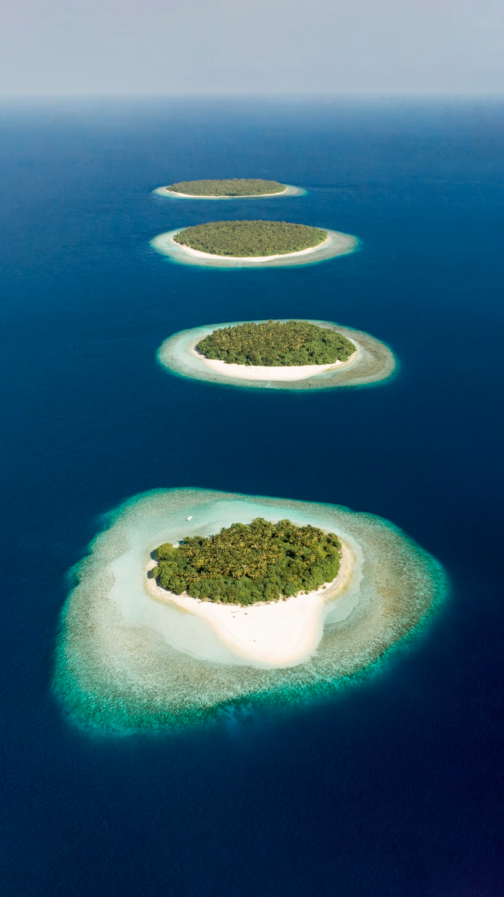 Aerial view of four small tropical islands with dense green vegetation surrounded by turquoise shallow waters and deep blue ocean.