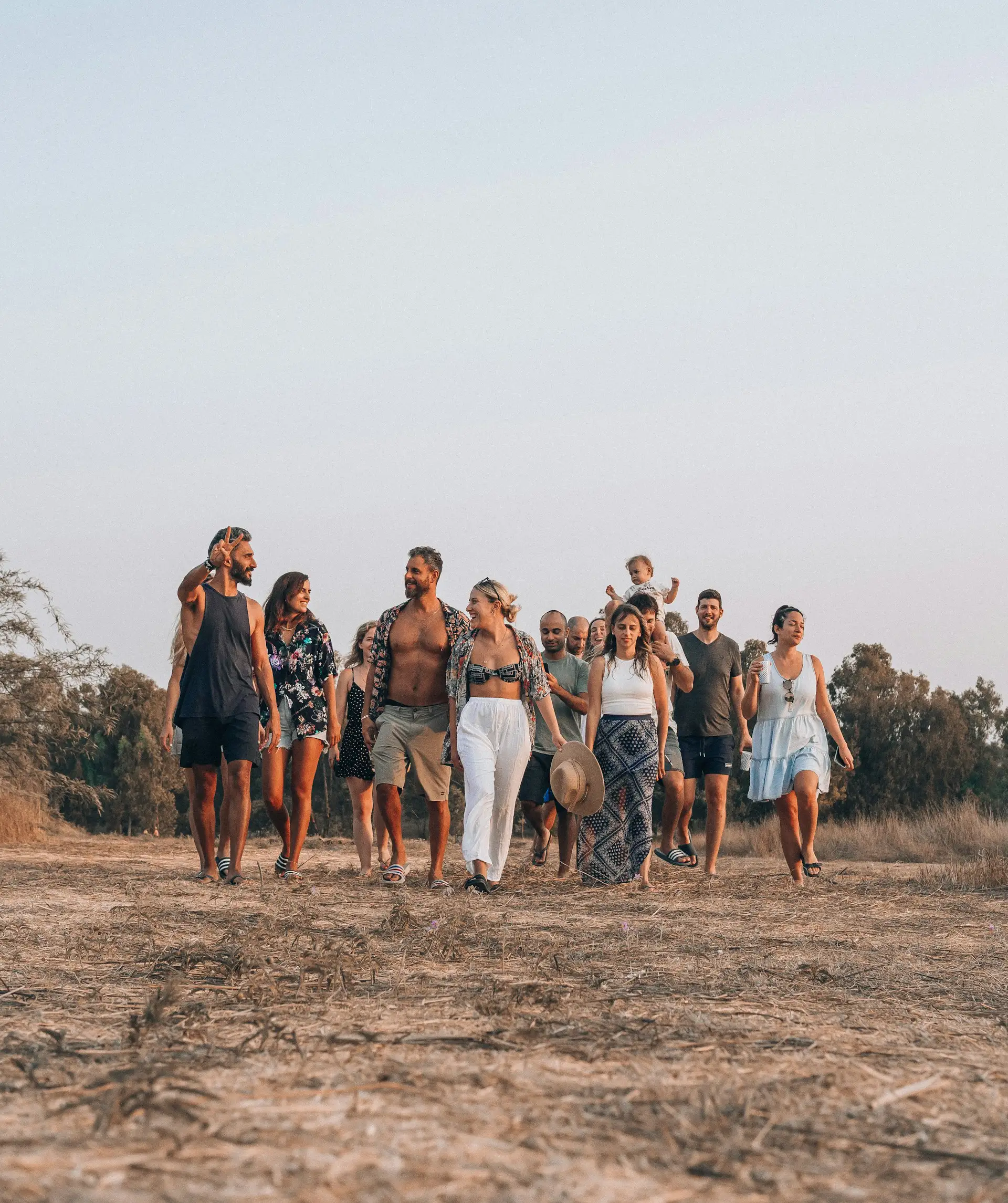 Group of diverse friends walking together outdoors on a dry grassy field during sunset, smiling and enjoying each other's company.