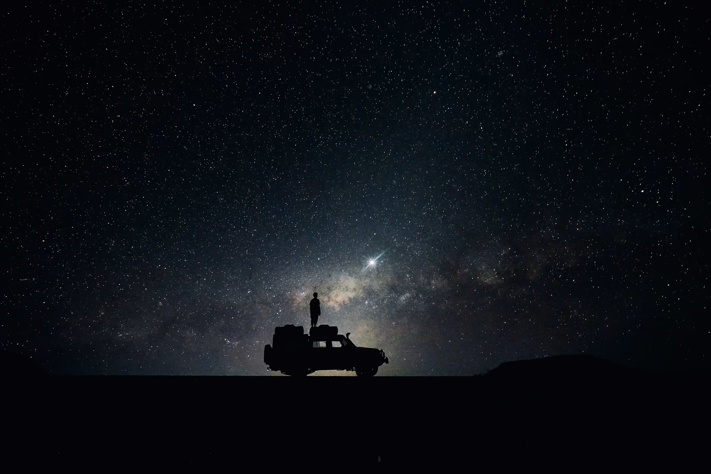 Silhouette of a person standing on a vehicle under a star-filled night sky with the Milky Way visible.
