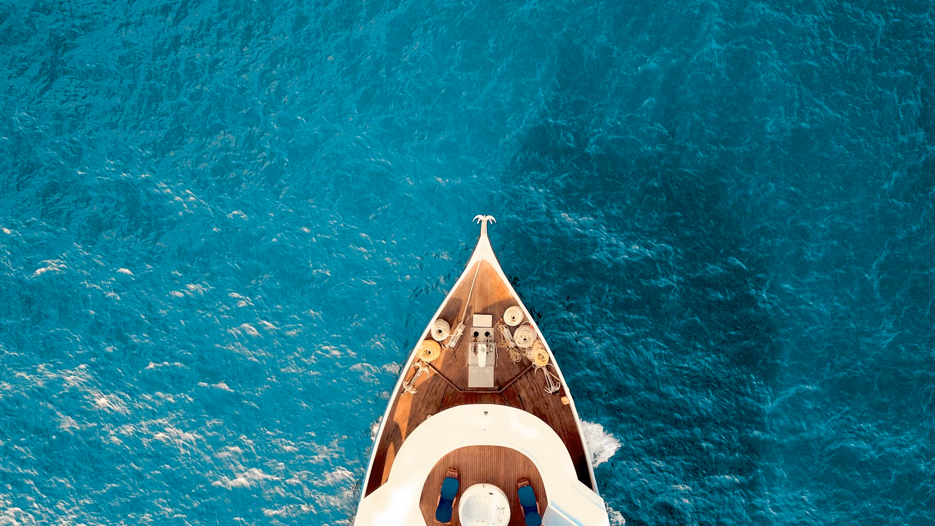 Aerial view of the bow of a white yacht cruising in clear blue water.