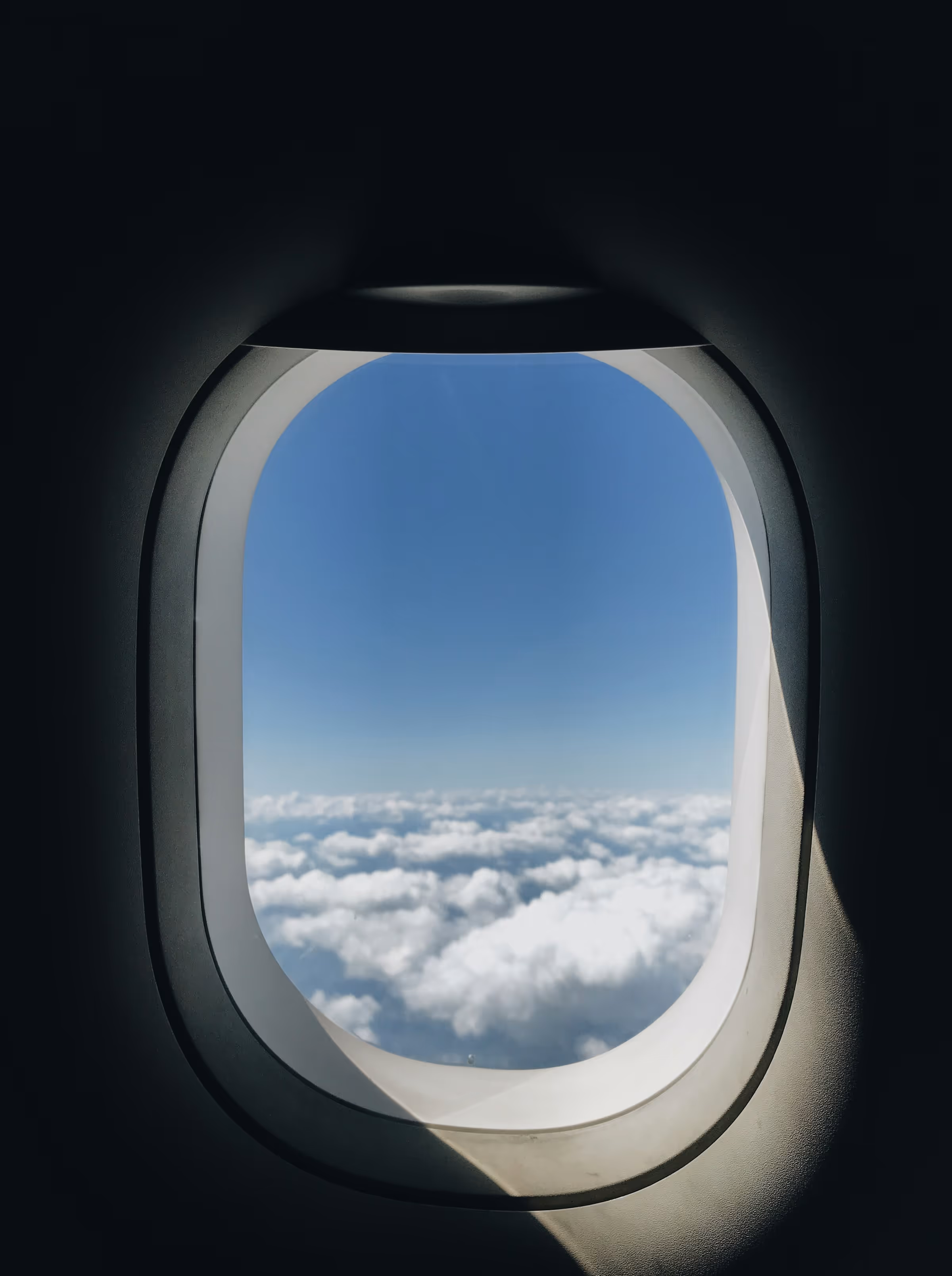View of blue sky and white clouds seen through an airplane window.