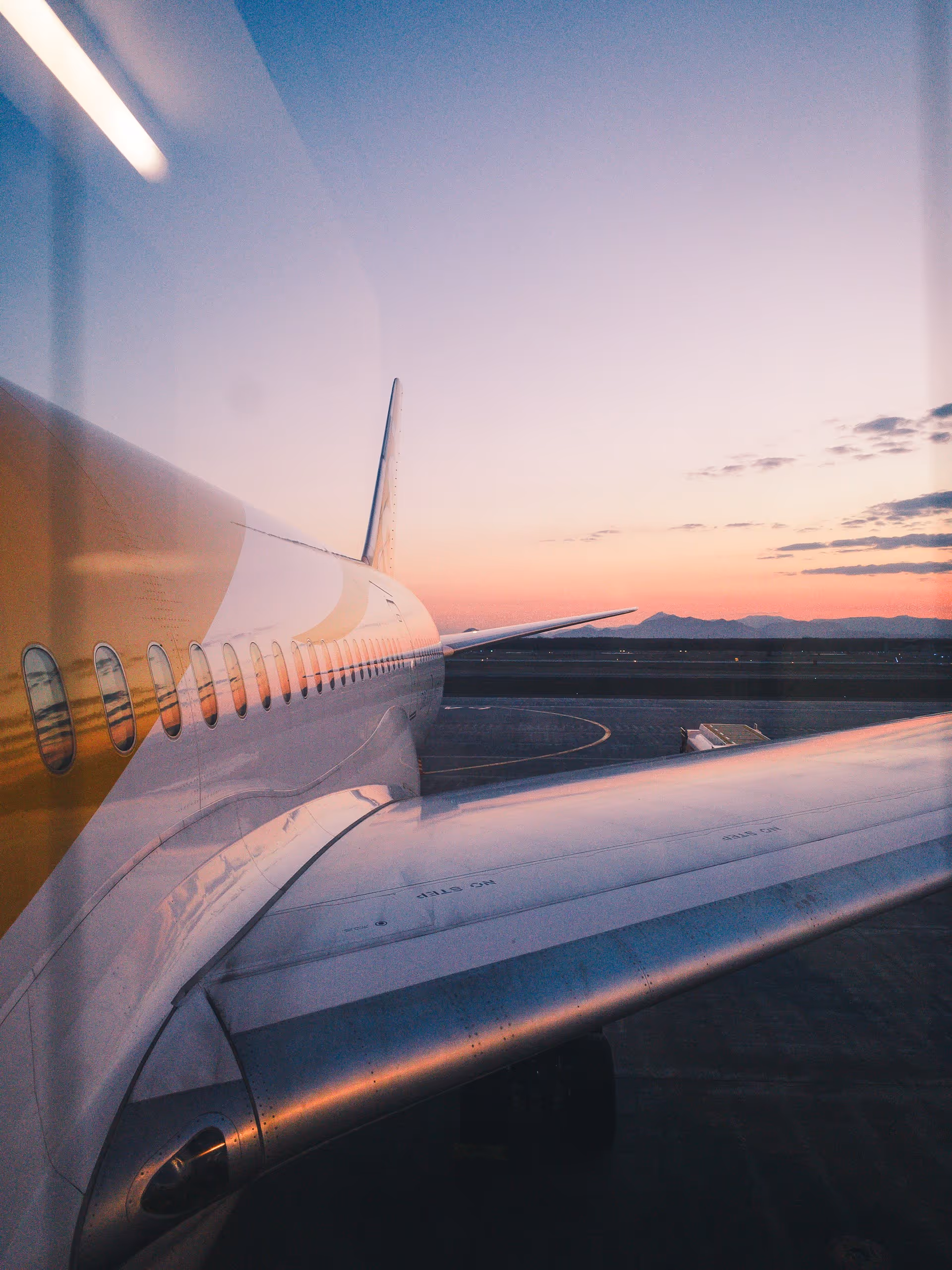 View of an airplane wing and fuselage at sunset from the passenger window.
