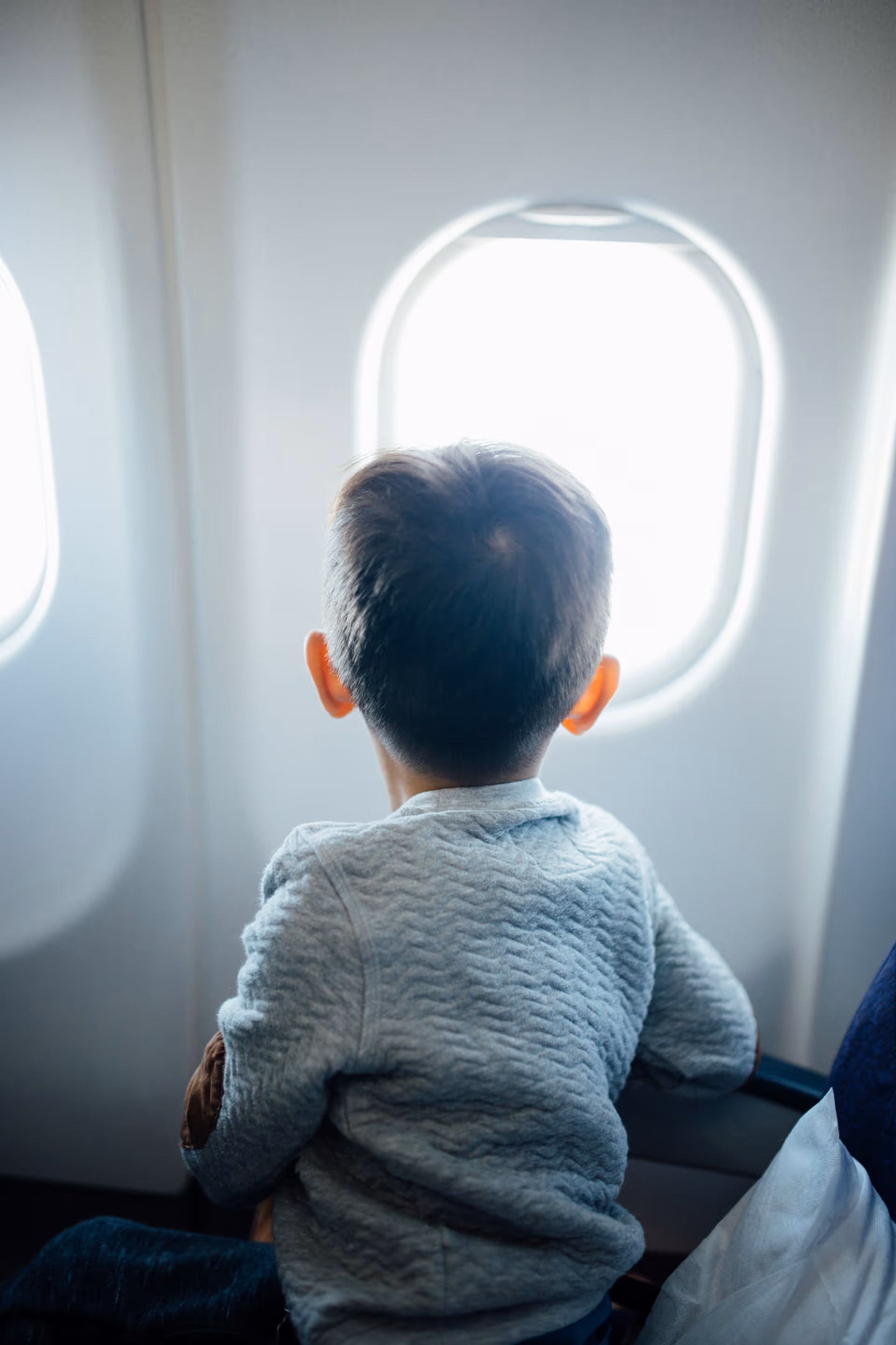 Young child in a gray sweater looking out an airplane window.