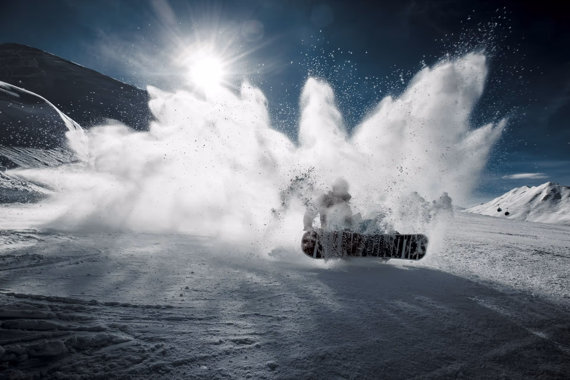 Snowboarder kicking up a large spray of snow on a sunny mountain slope.