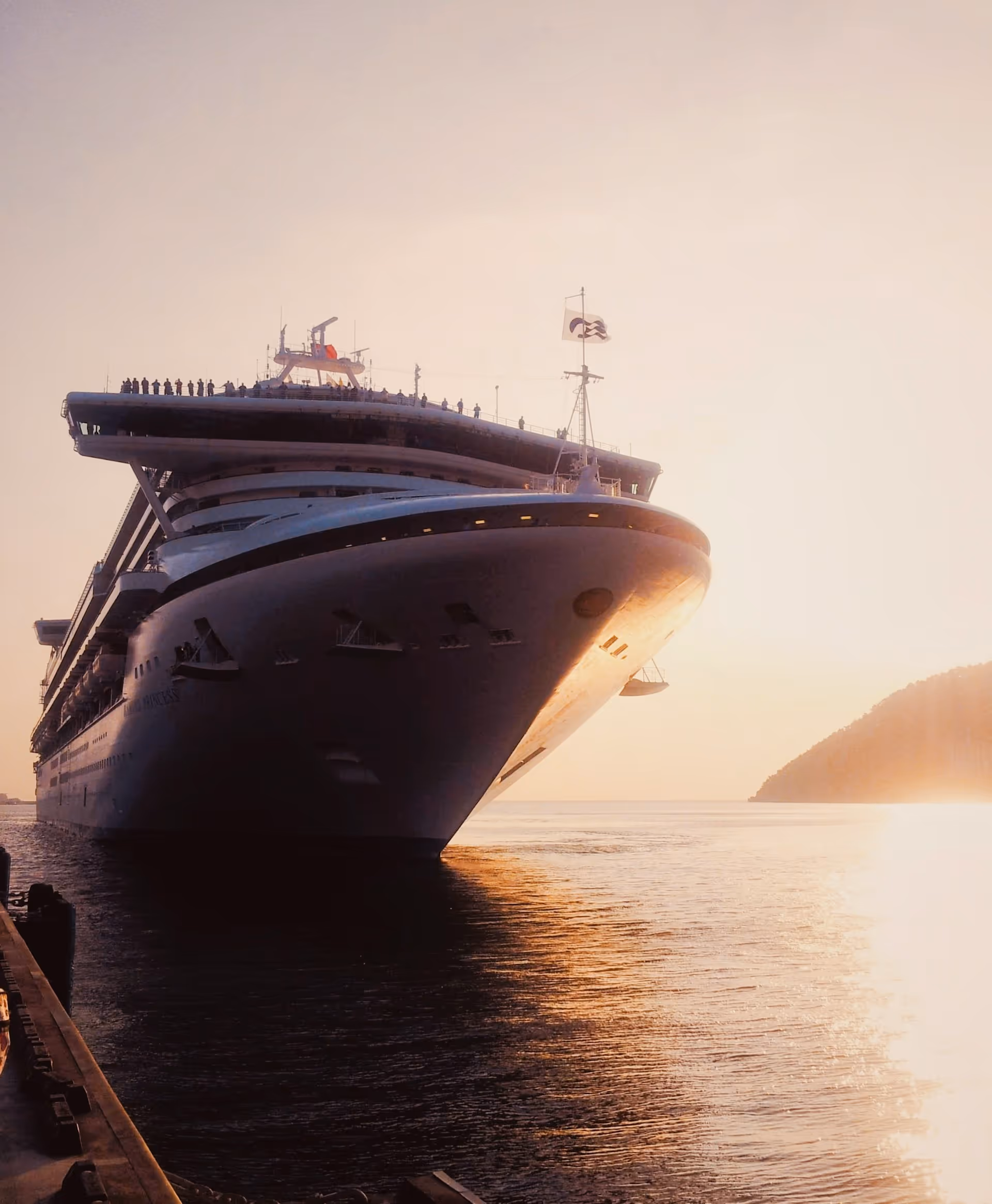 Large cruise ship docked at sunset with warm sunlight reflecting on the water.