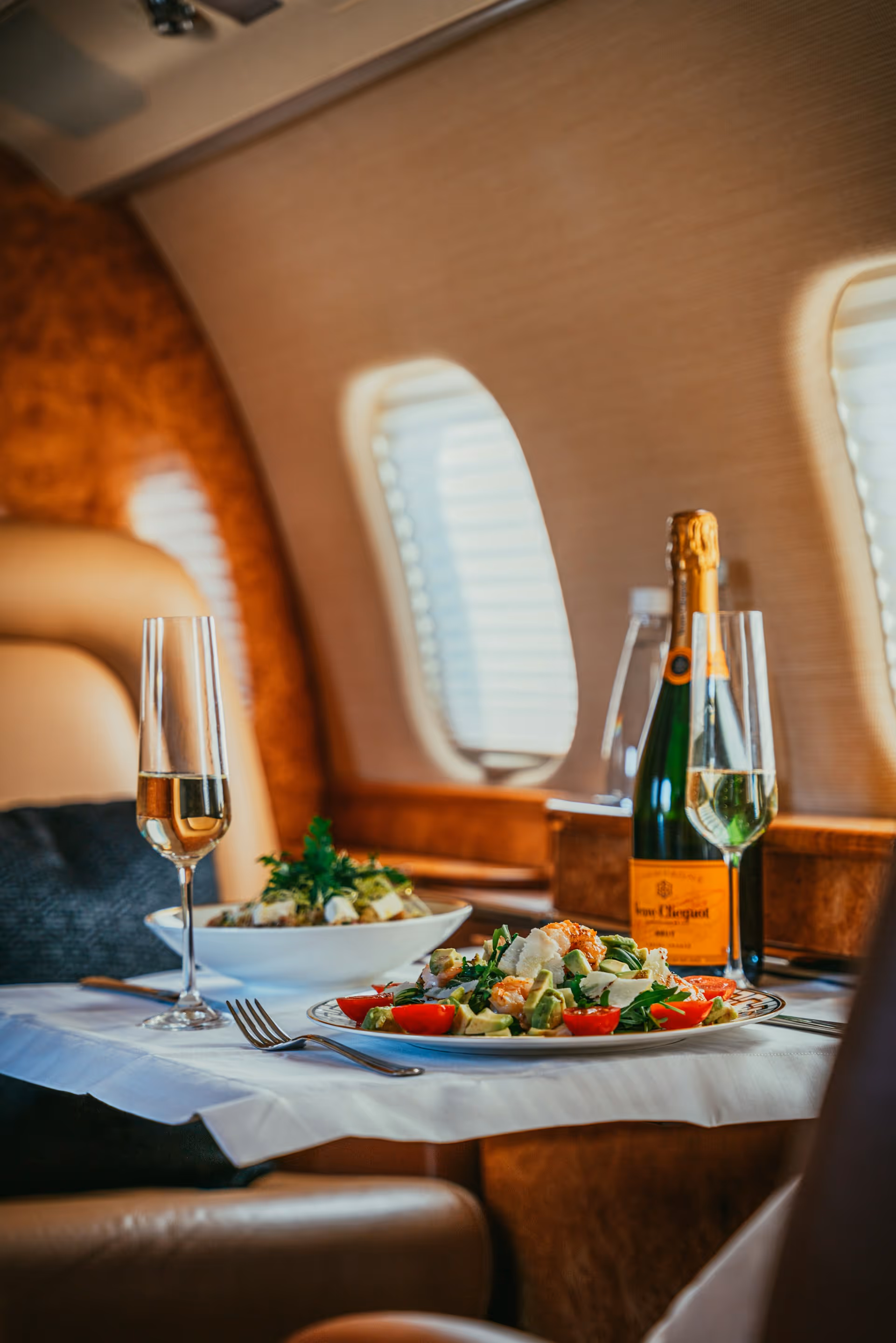 Champagne bottle and glasses with plates of salad served on a table inside a private jet.