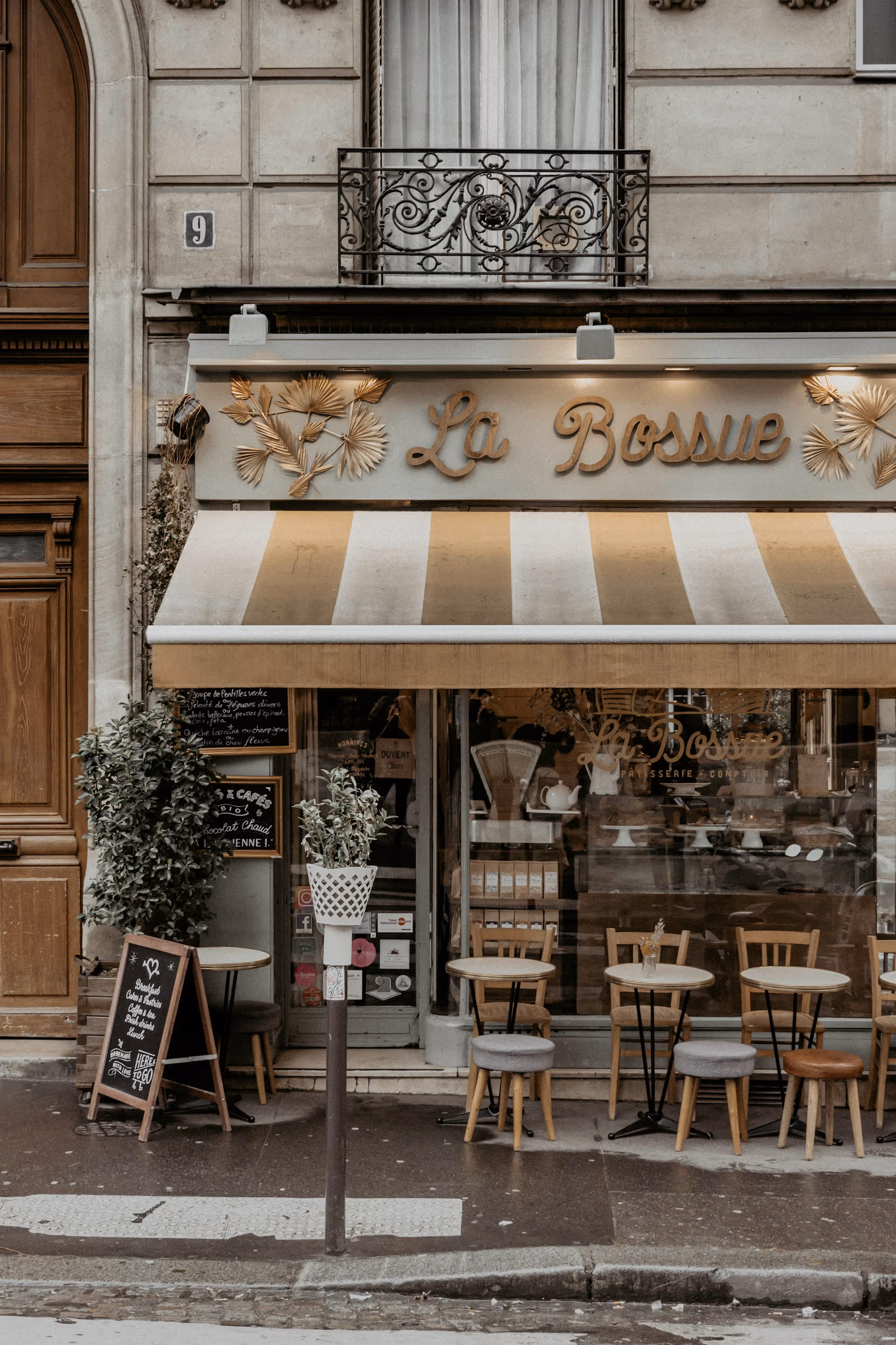 Outdoor seating of La Bossue café with small round tables, various chairs, a striped awning, and decorative gold lettering on the facade.