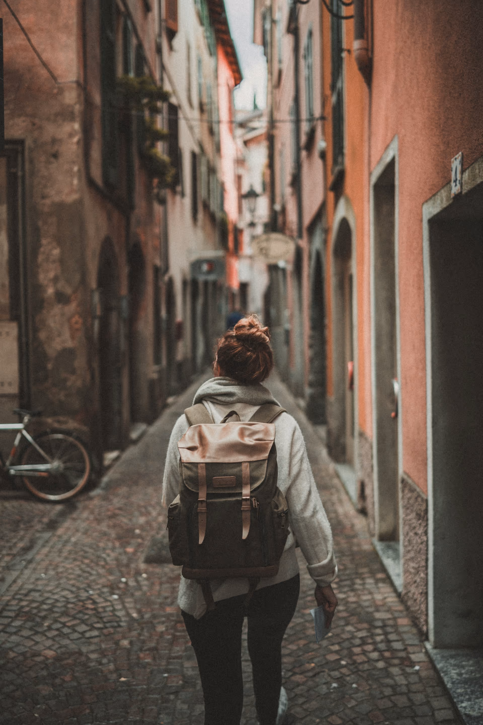 Person with a backpack walking down a narrow cobblestone street between tall buildings.