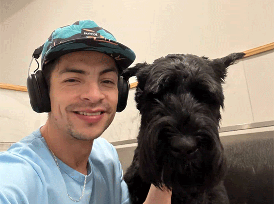 Marc Groomer wearing a green hat with headphones with a light blue tee with a black poodle