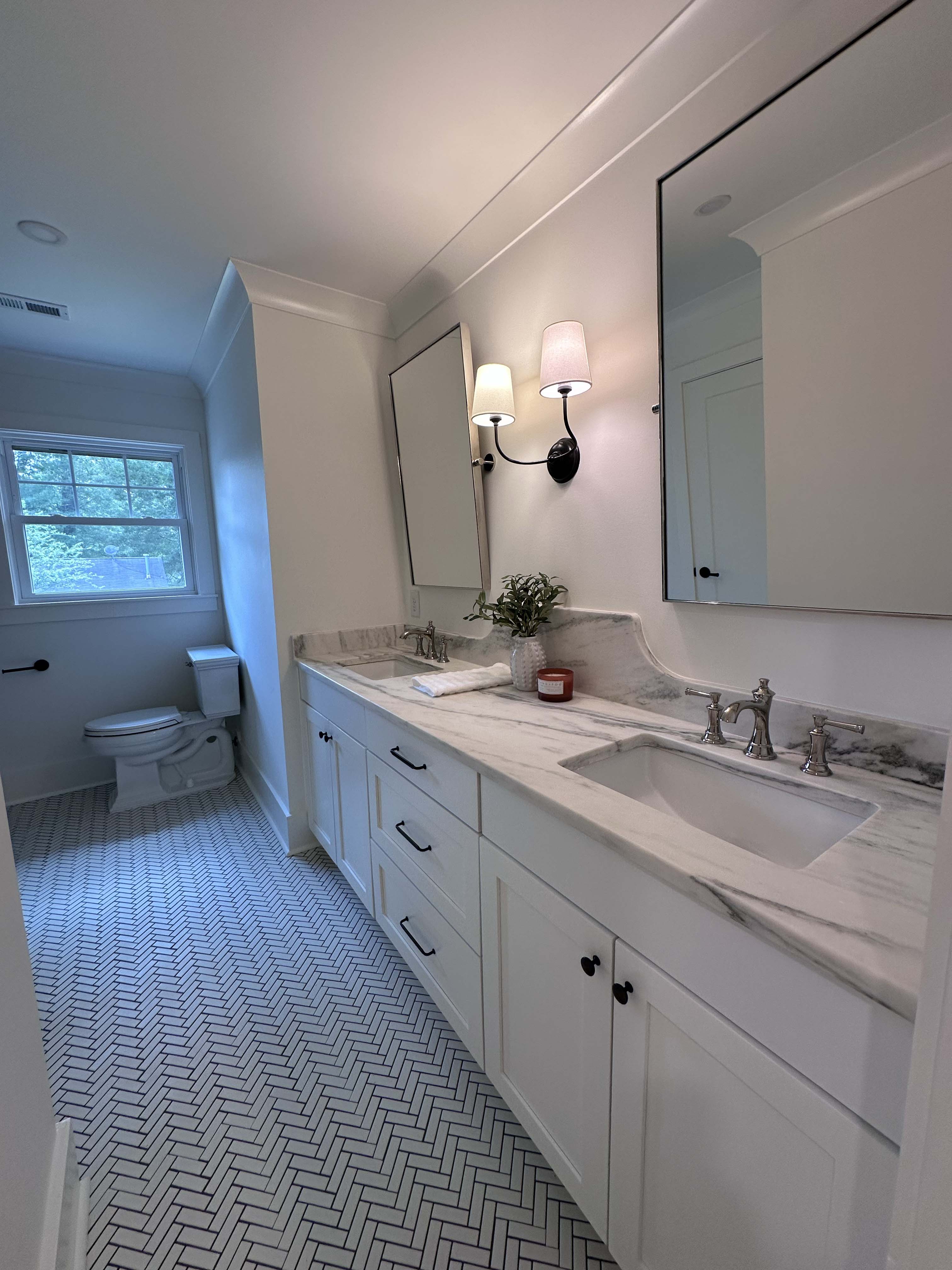 Modern bathroom with white marble double sink vanity, large mirror, wall sconces, and patterned tile floor.