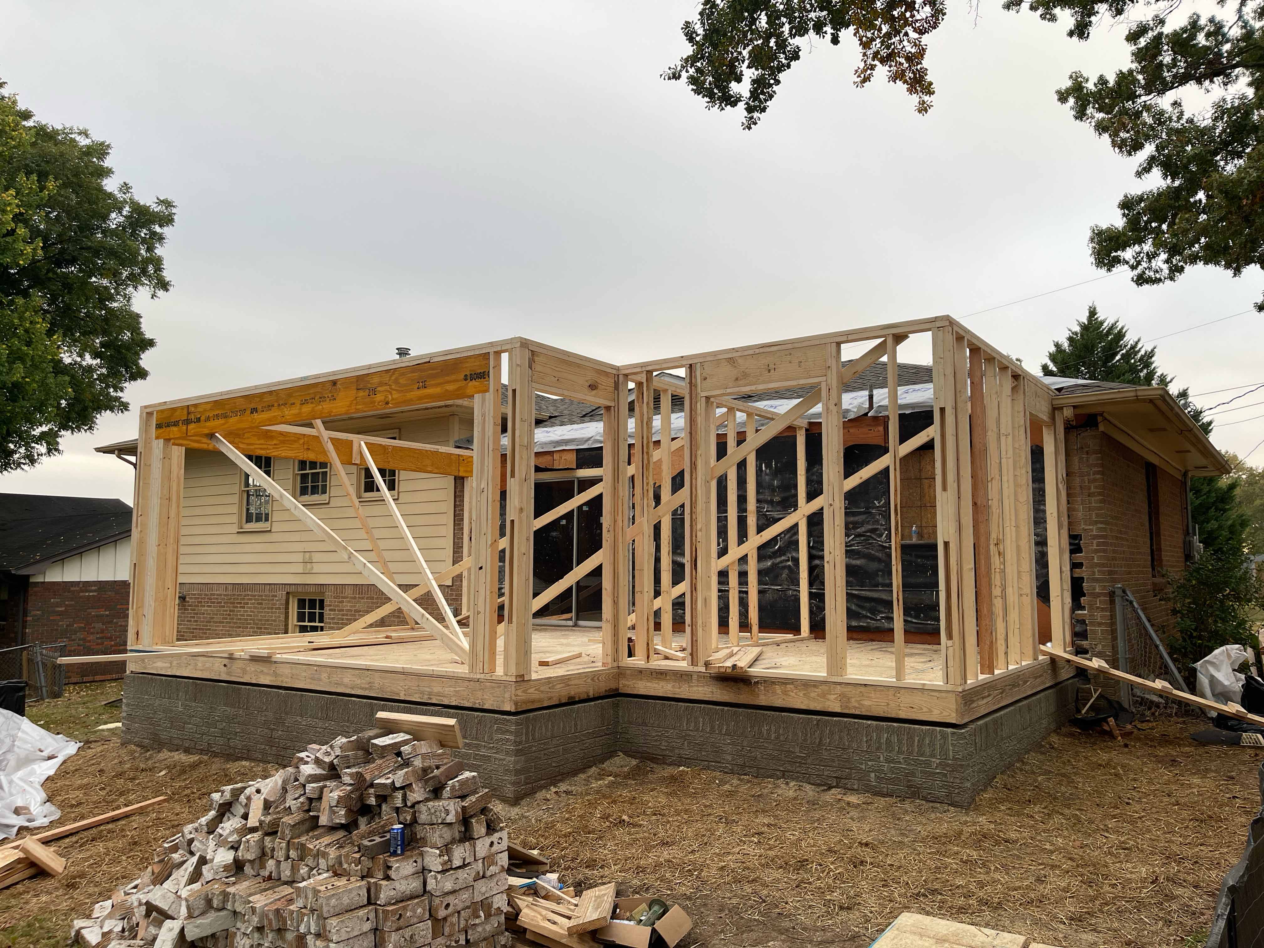 Wooden framework of a house extension under construction next to an existing brick and siding house.