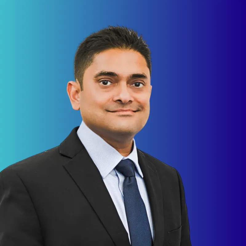 Portrait of a man in a black suit, light blue shirt, and navy tie against a blue gradient background.