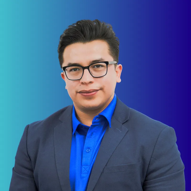 Portrait of a man with black hair and glasses wearing a blue shirt and dark blazer on a blue gradient background.